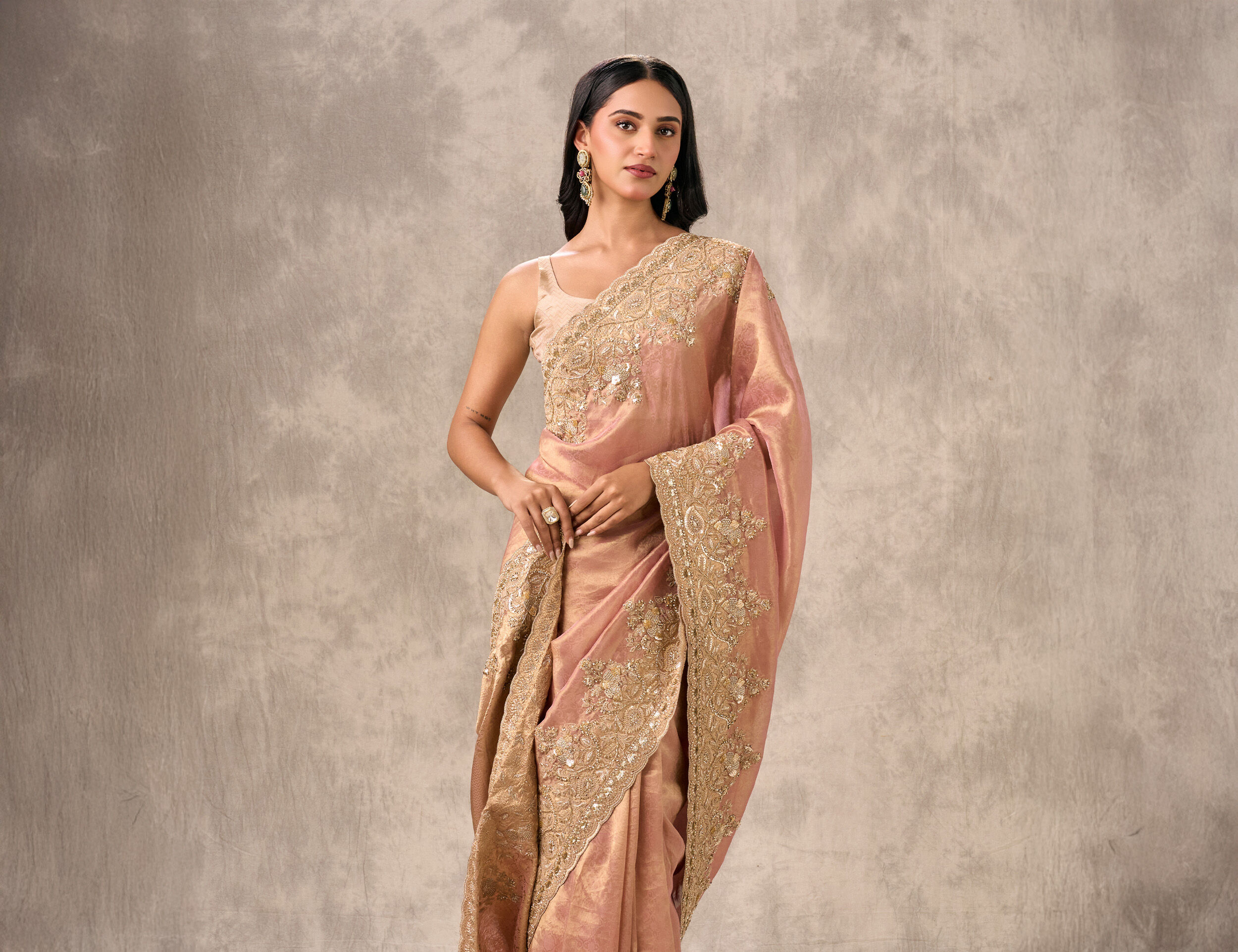 Woman in a shimmering dusky pink silk saree with heavy gold zari embroidery along the border and pallu.
